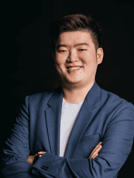 A portrait of Hermanto Wie, one of Topremit's co-founders, smiles confidently in a dark grey suit with his arms crossed.