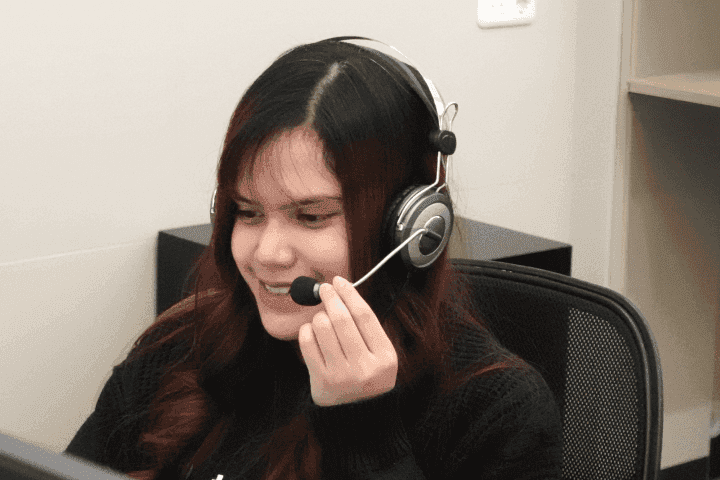 A long-haired woman wearing a Topremit t-shirt is smiling while wearing headphones.