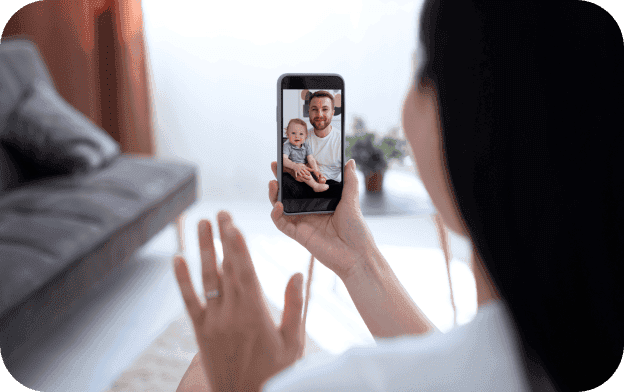 A woman holding a smartphone with a man and a baby displayed on its screen.