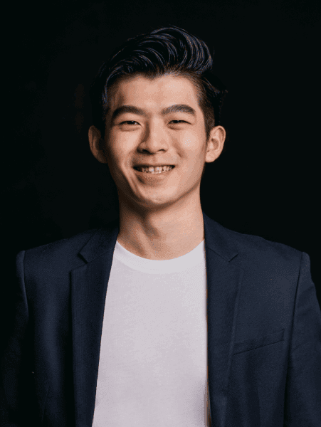 Topremit の共同設立者の一人、Henry Wirawan氏が、白い T シャツの上に黒いスーツを着て、自信に満ちた笑顔を浮かべているポートレート。