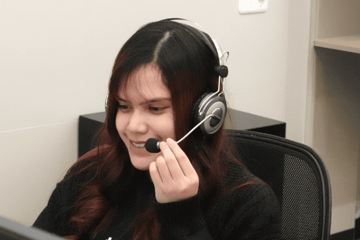 Topremit の T シャツを着た長髪の女性が、ヘッドフォンを着けながら笑っています。
